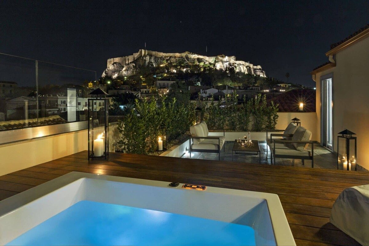 Private outdoor jacuzzi and terrace seating with the illuminated Acropolis behind.