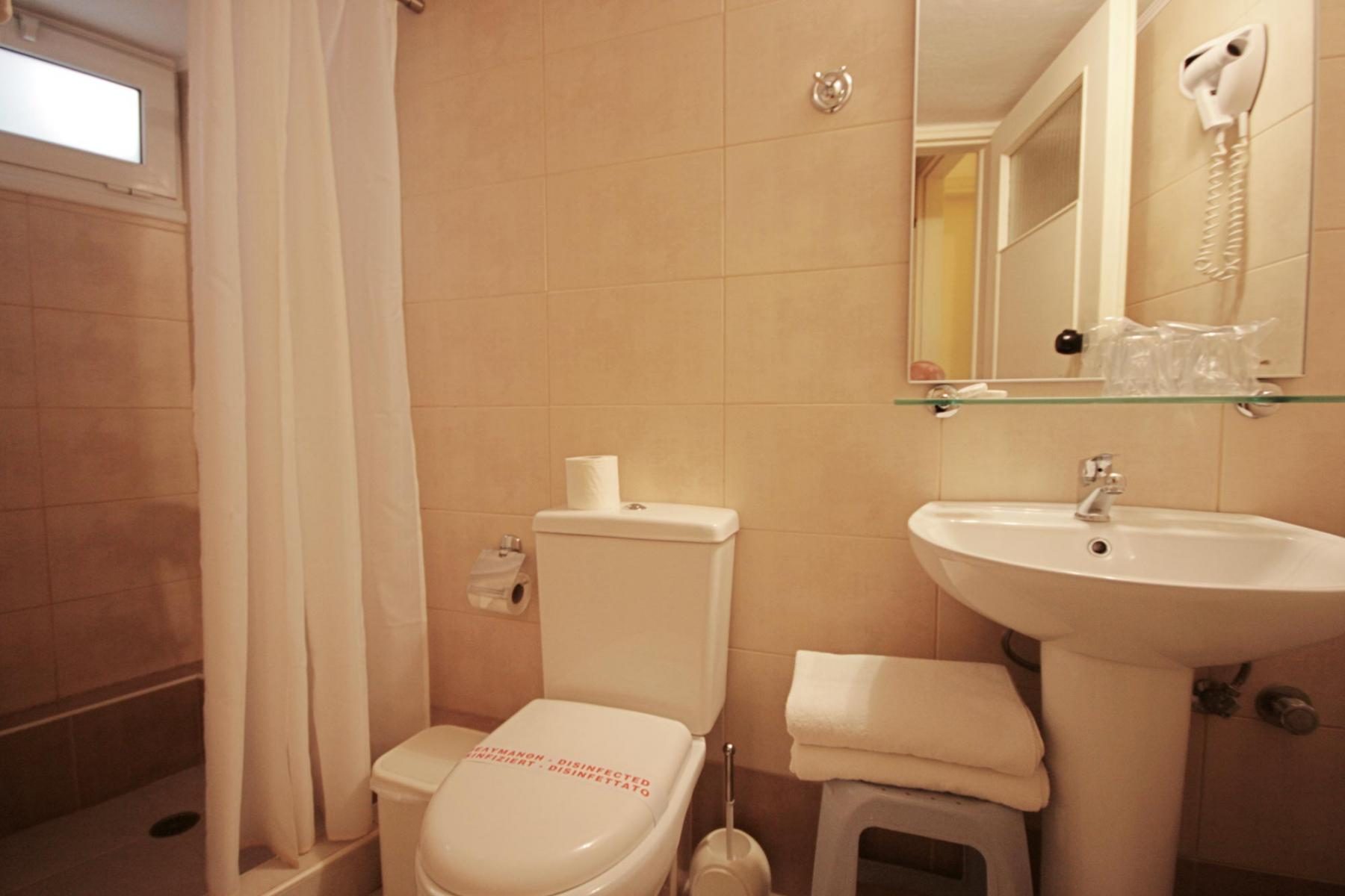 Compact bathroom with basin, toilet and curtained shower area.
