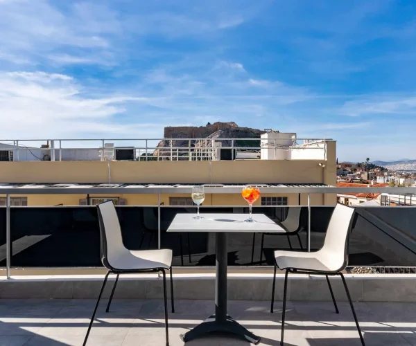 Two chairs and a small table with drinks, with the Acropolis beyond the railing.