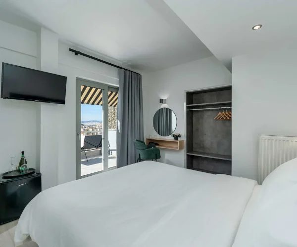 White bed beside a balcony doorway, with wall-mounted television and open wardrobe.