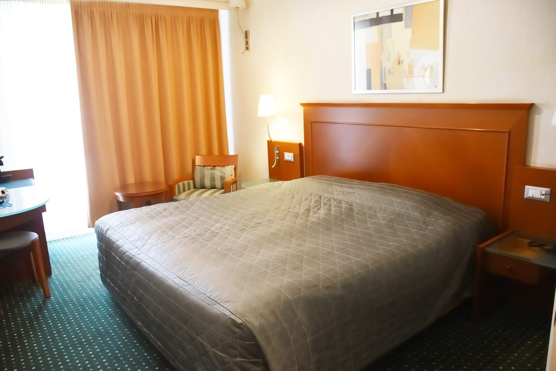 Double bed, wooden headboard and curtains in Adrian Hotel’s Acropolis View room.
