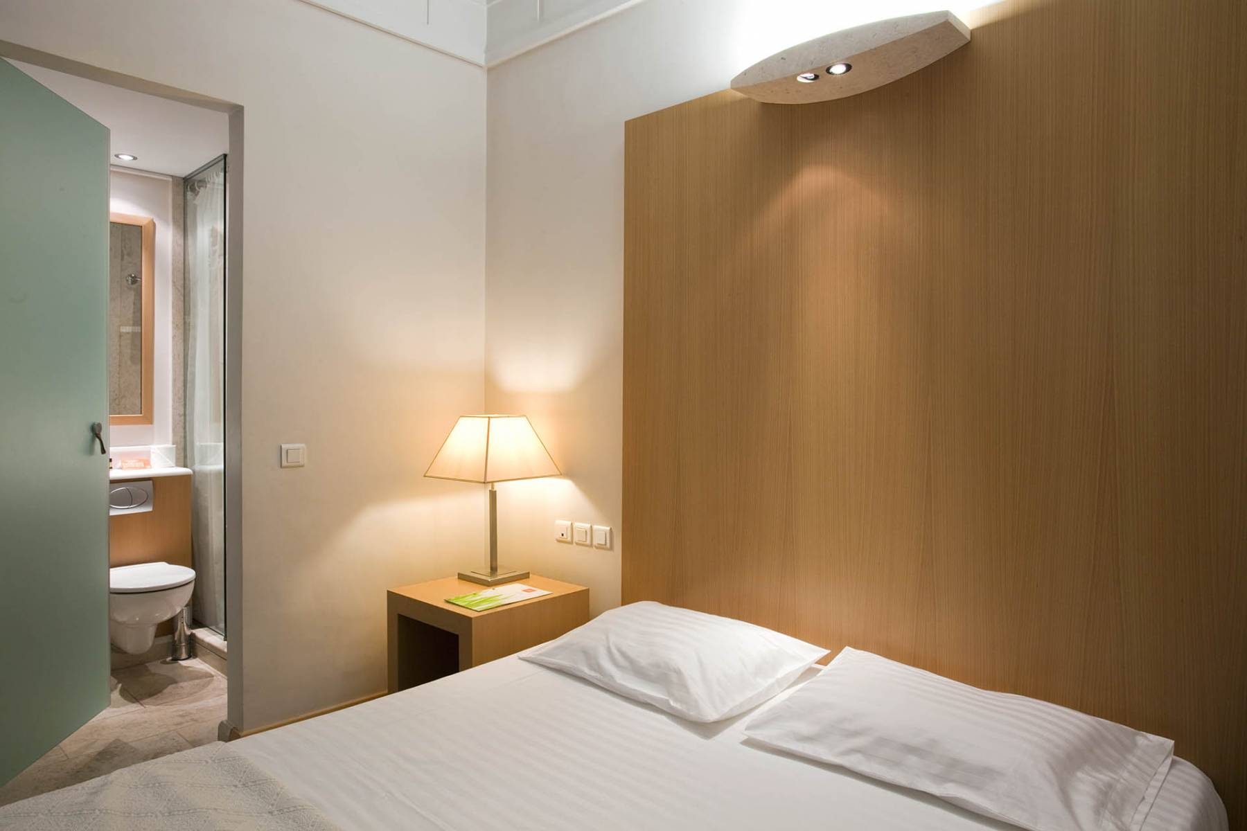 Bed and bedside lamp beside an open bathroom doorway in Central’s Family Room gallery.