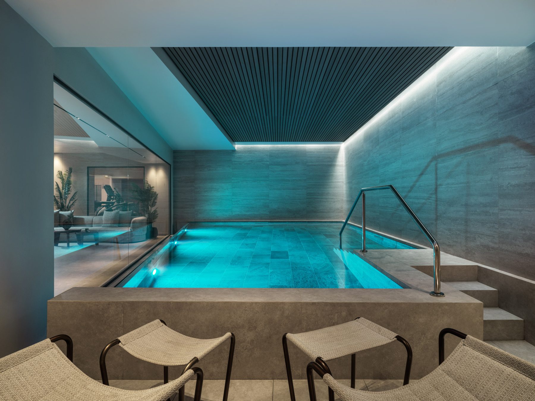 Indoor pool with blue lighting, stone walls and metal handrail.