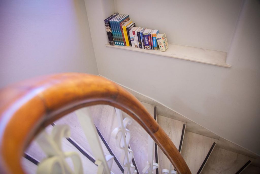 Curving wooden handrail and hotel stairwell beside a small bookshelf.