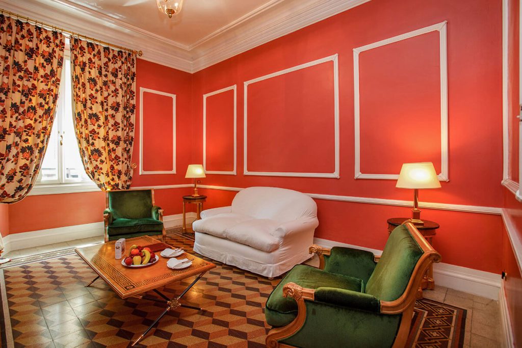 White sofa and green armchairs around a low table in a red-walled room.