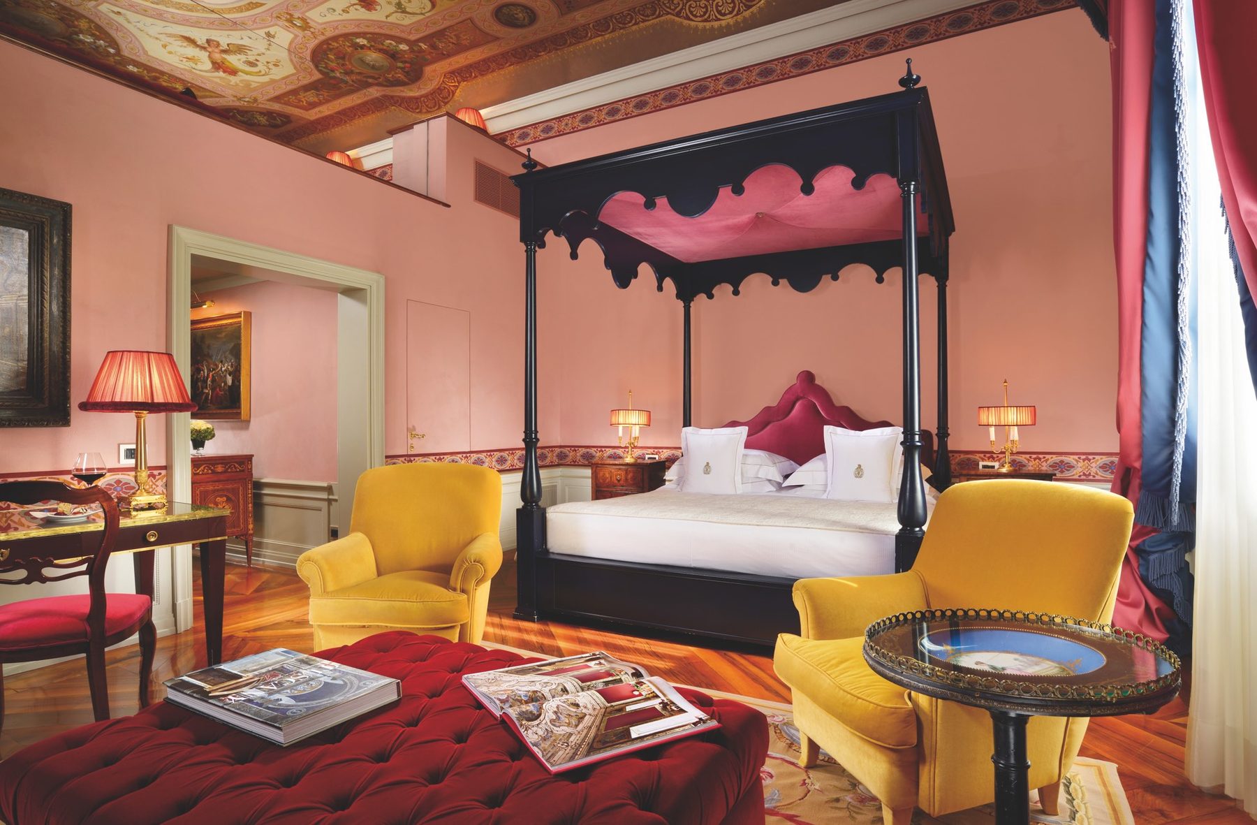Canopy bed and yellow armchairs beneath a frescoed ceiling.