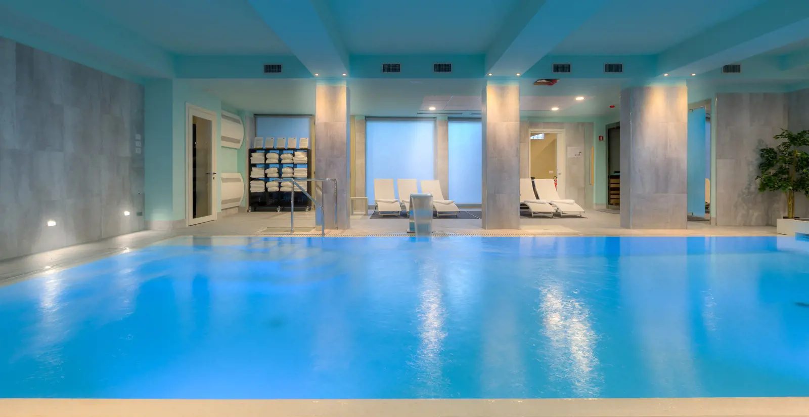 Indoor swimming pool with loungers and towel shelves beyond.