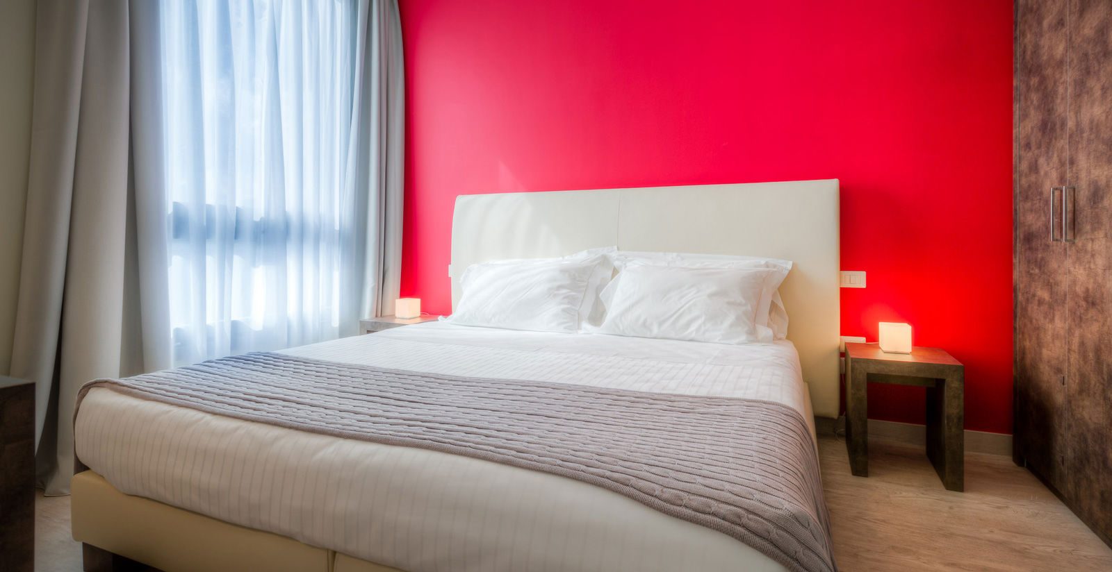 Double bed against a red wall beside a curtained window.