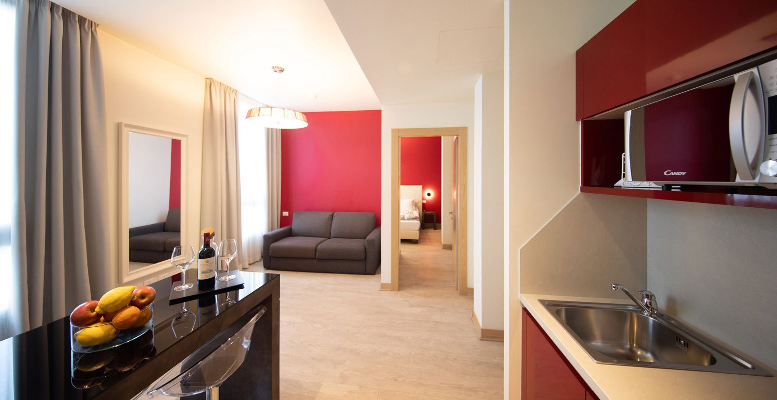 Red kitchen cabinets and a microwave beside a living room with a sofa.