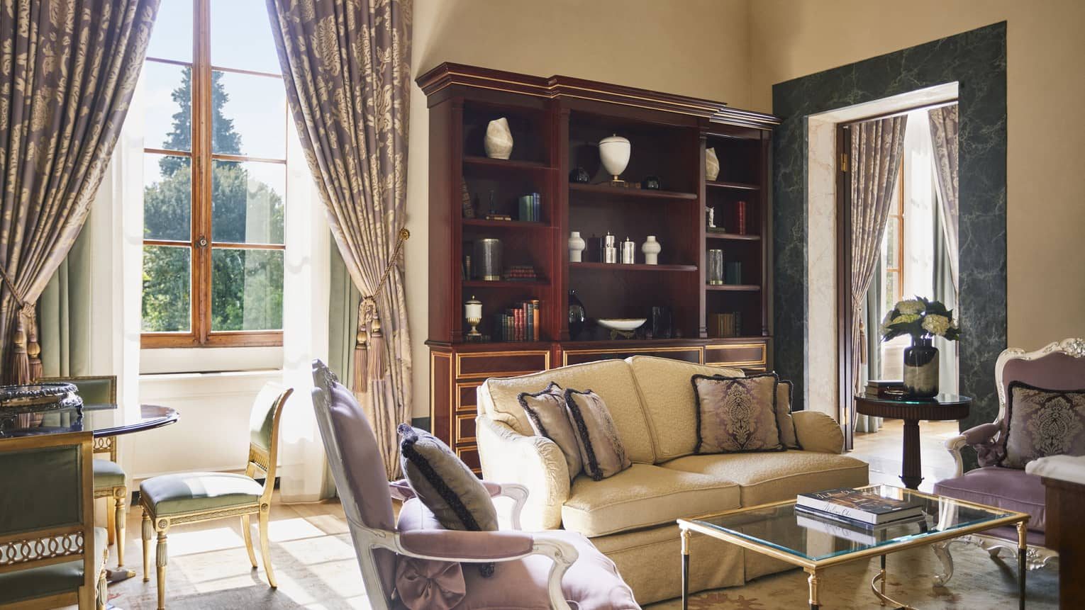 Sofa and armchairs beside tall windows and wooden shelves.