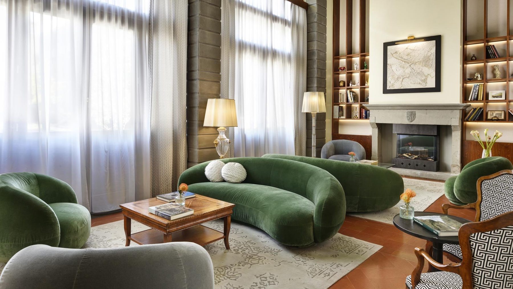 Green sofas and low tables beside a fireplace and illuminated shelves.