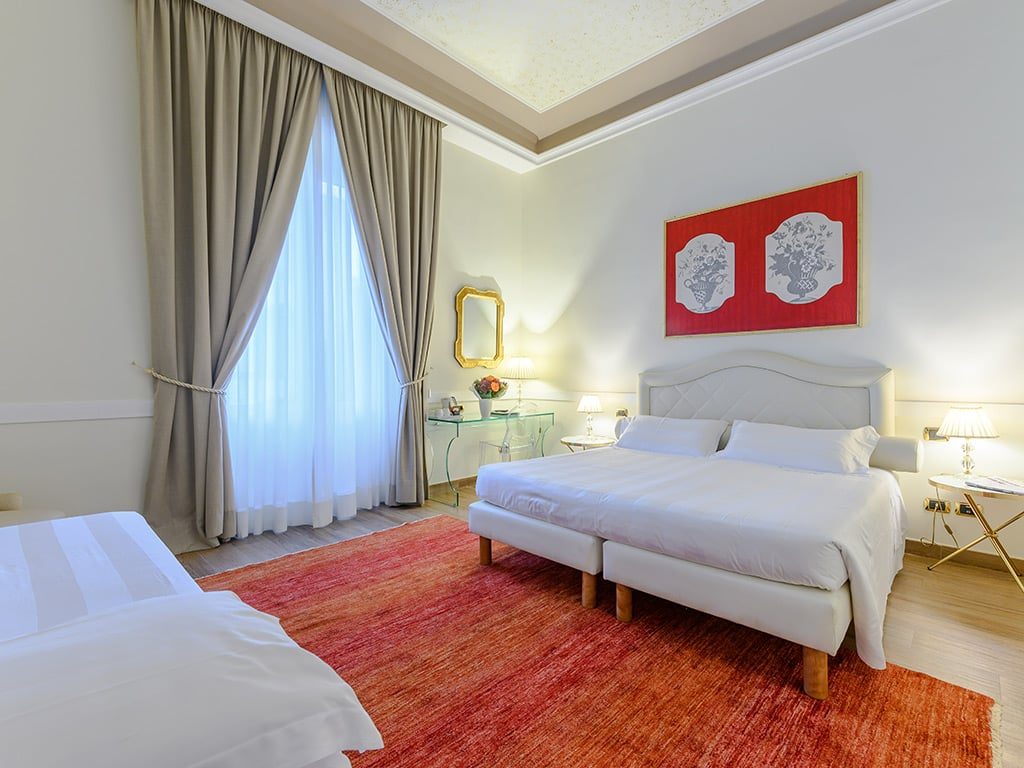 Twin beds with white bedding and a red rug in a light-coloured room.