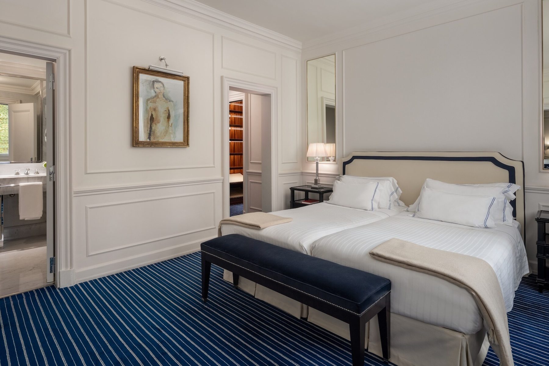 White bedroom with blue-striped carpet and a doorway to the bathroom.