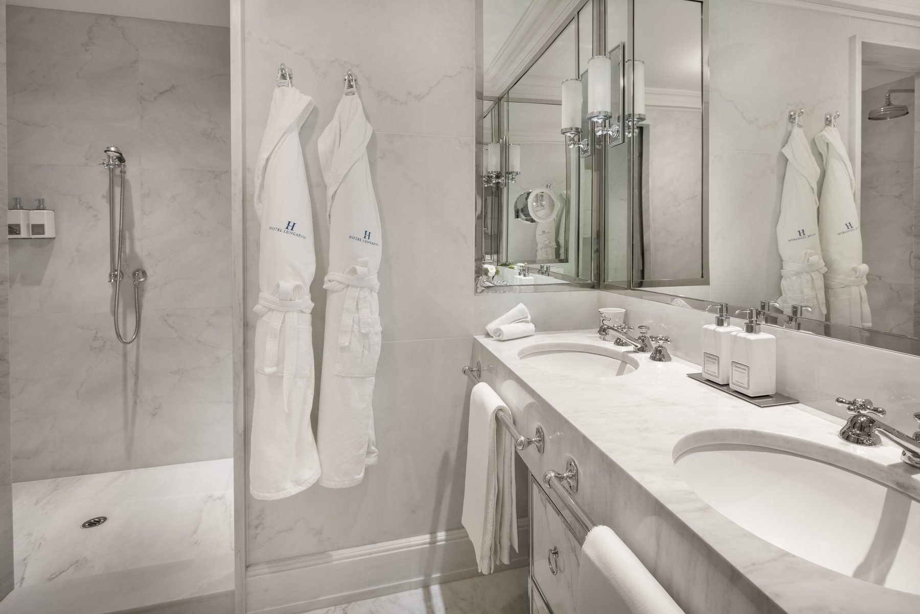 Marble shower bathroom with two basins and hanging bathrobes.