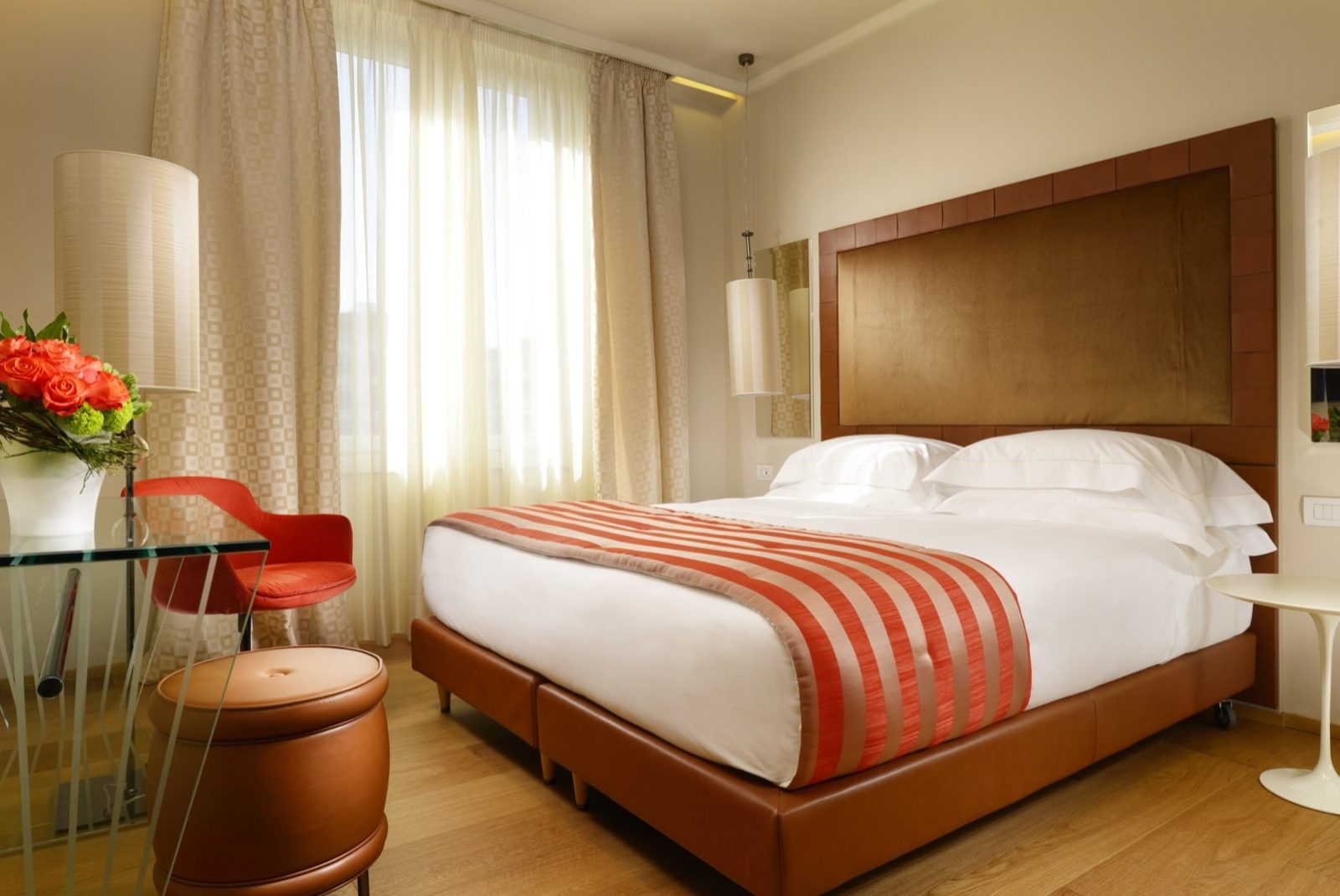 Bedroom with an orange-striped bed runner and a round glass table beside the window.