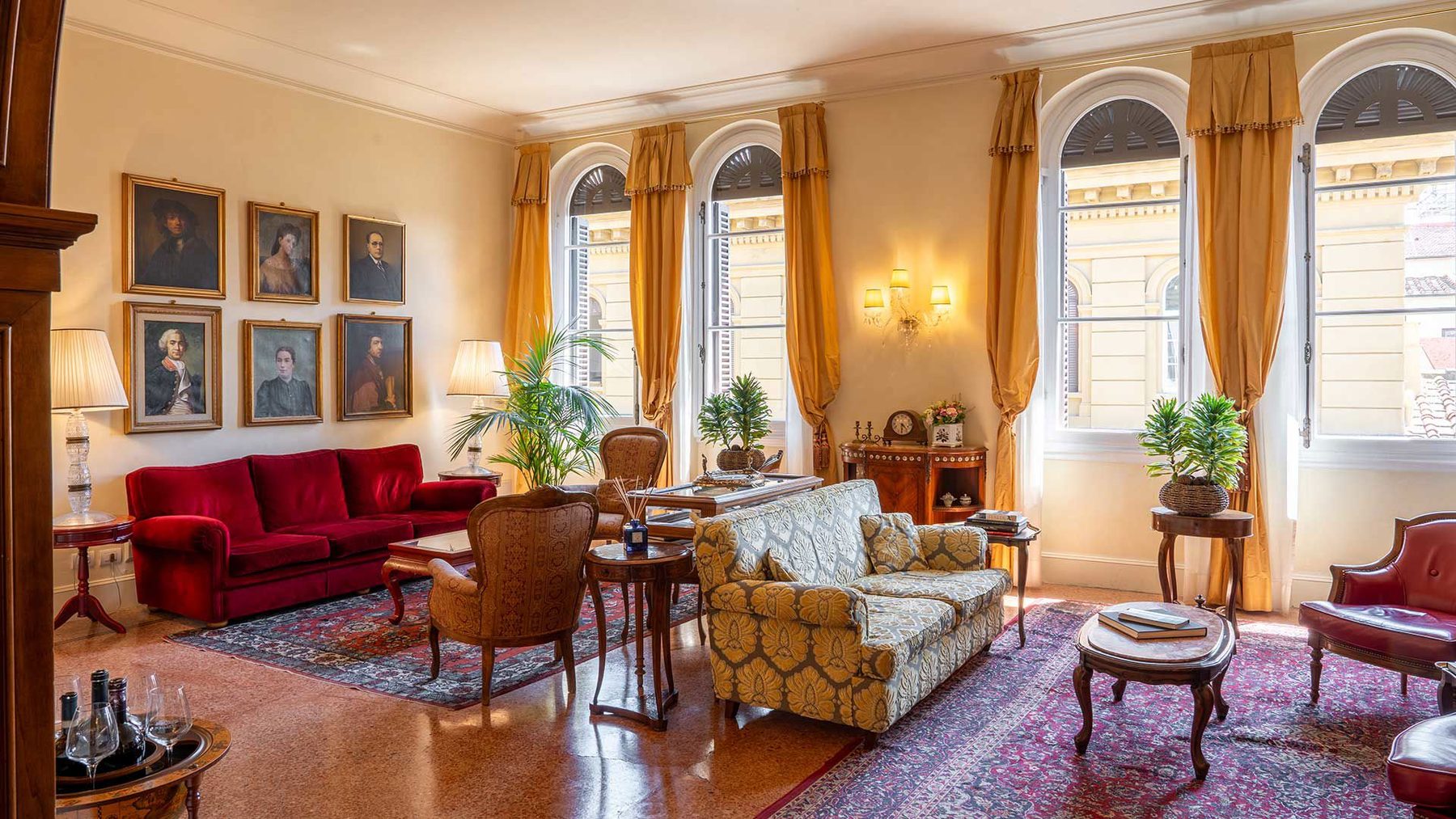 Sofas and armchairs beneath portraits in a sitting room with tall arched windows.