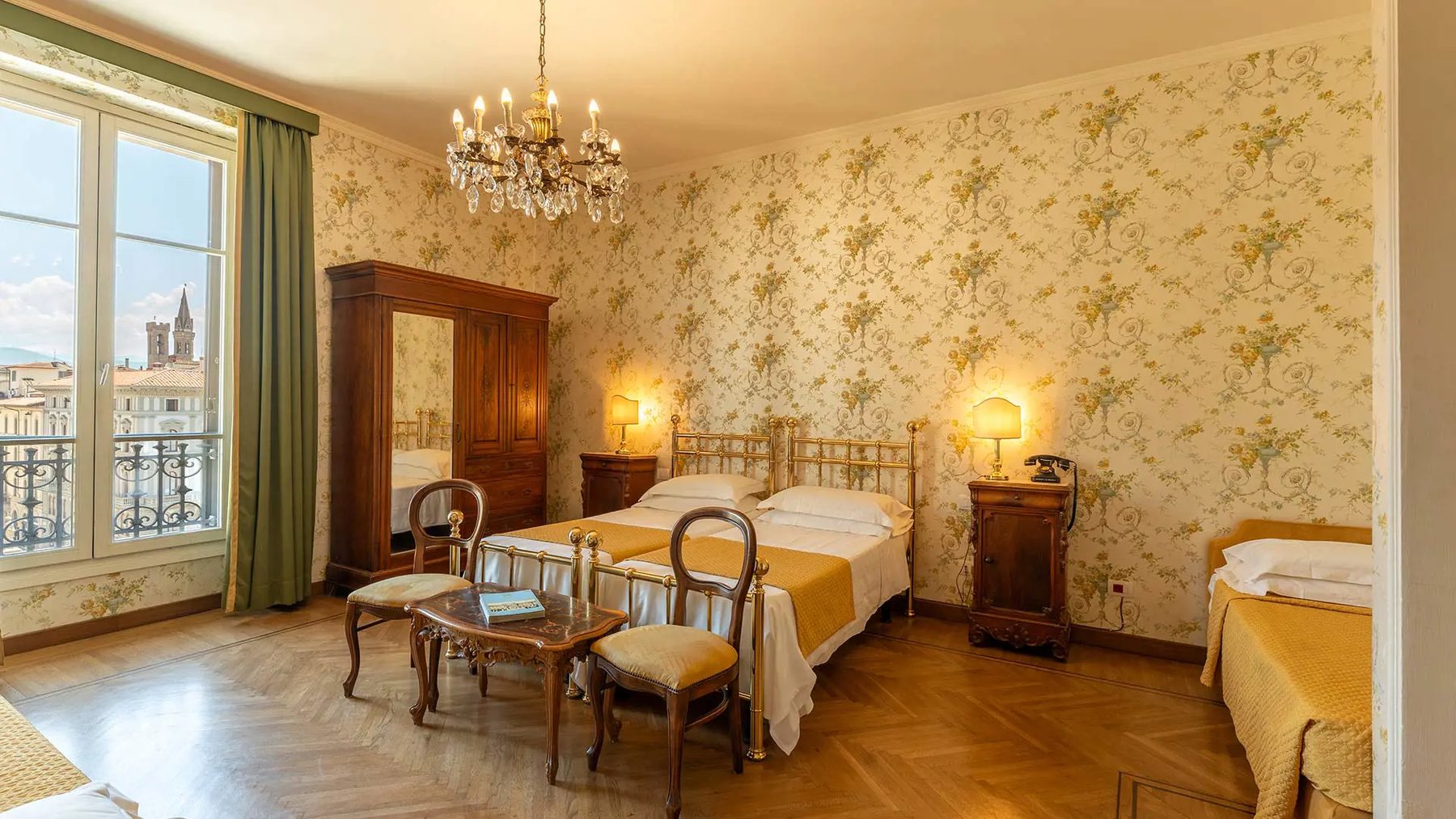 Floral-wallpaper bedroom with beds and a tall window overlooking the square.