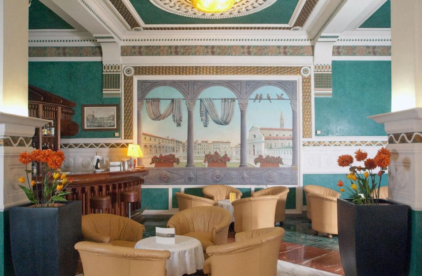 Cream armchairs and small tables in a lounge with green walls and painted panels.