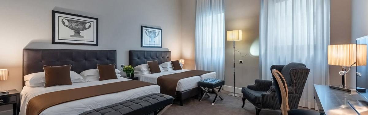 Two double beds with dark headboards beside a window.