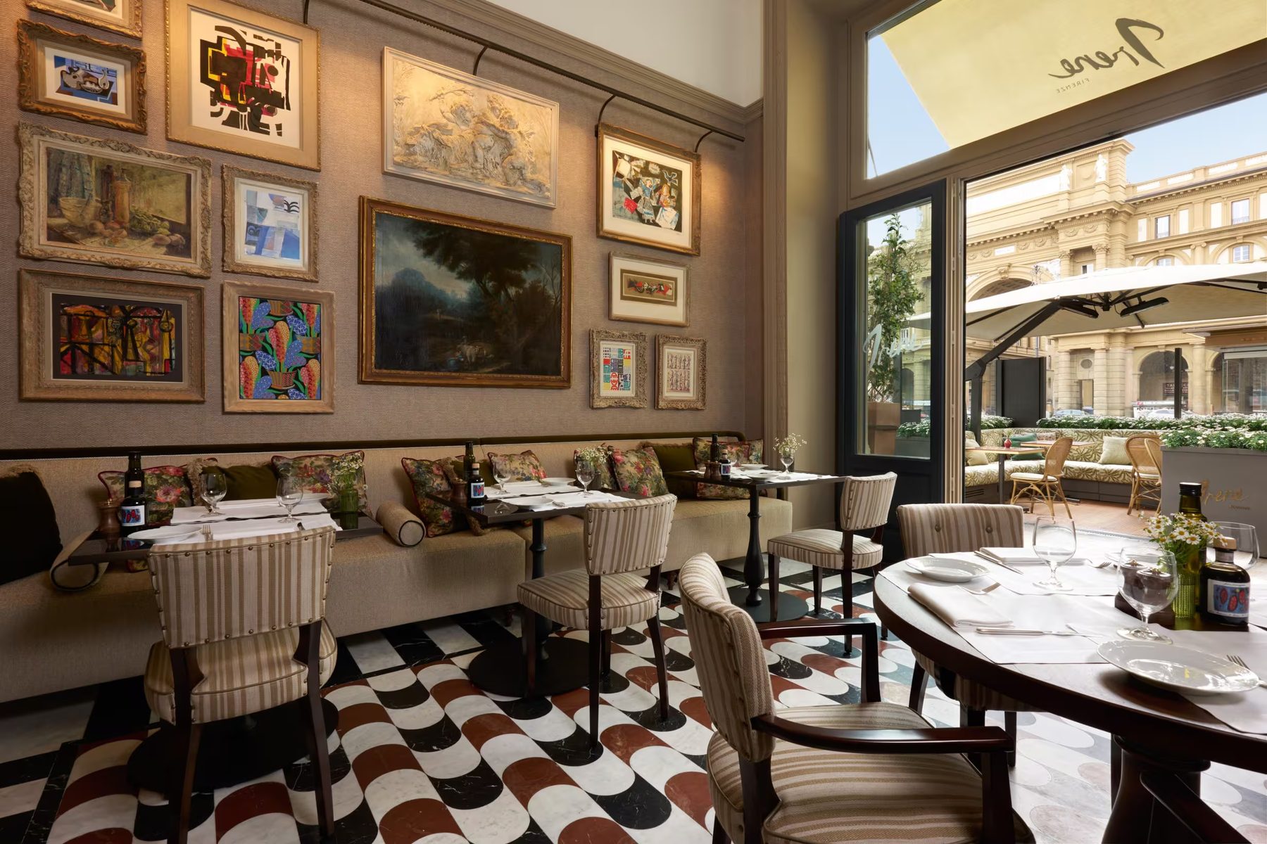 Dining tables and striped chairs beneath a picture-covered wall, with the terrace beyond.