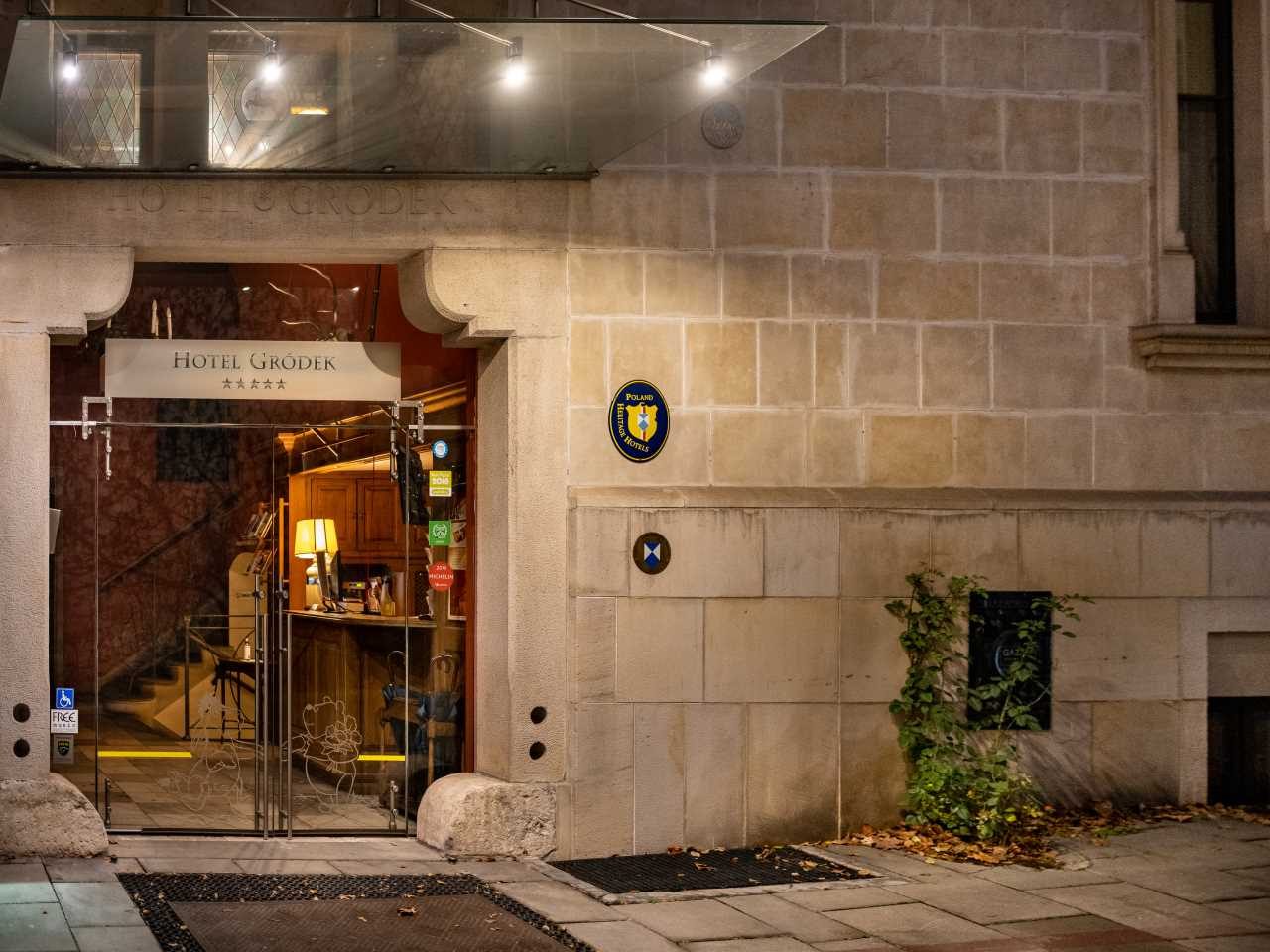Illuminated Hotel Gródek entrance in a stone façade.