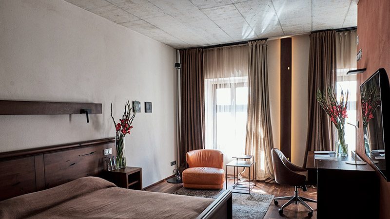 Hotel Stary bedroom with a dark wood bed, orange armchair and desk.