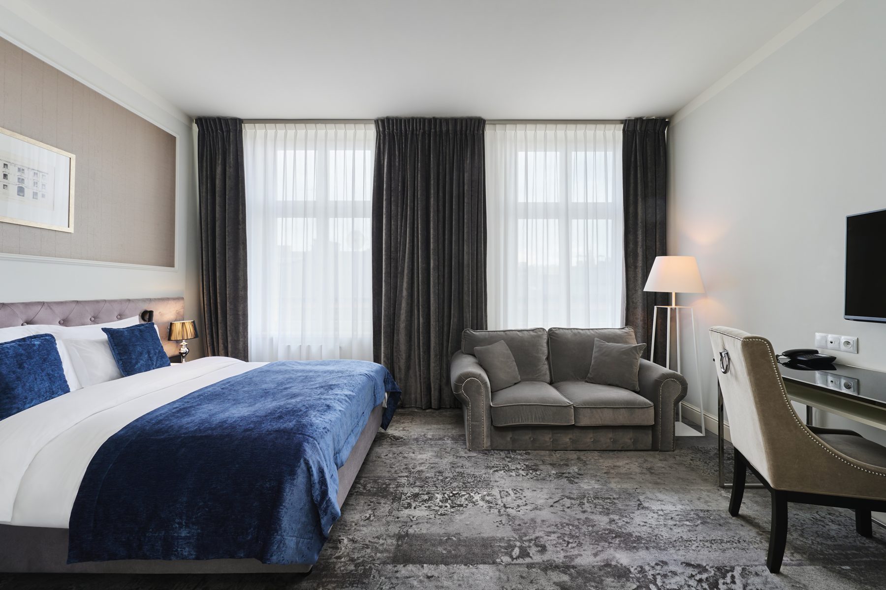 Wyndham Grand Premium bedroom with blue bedding, grey sofa and desk.