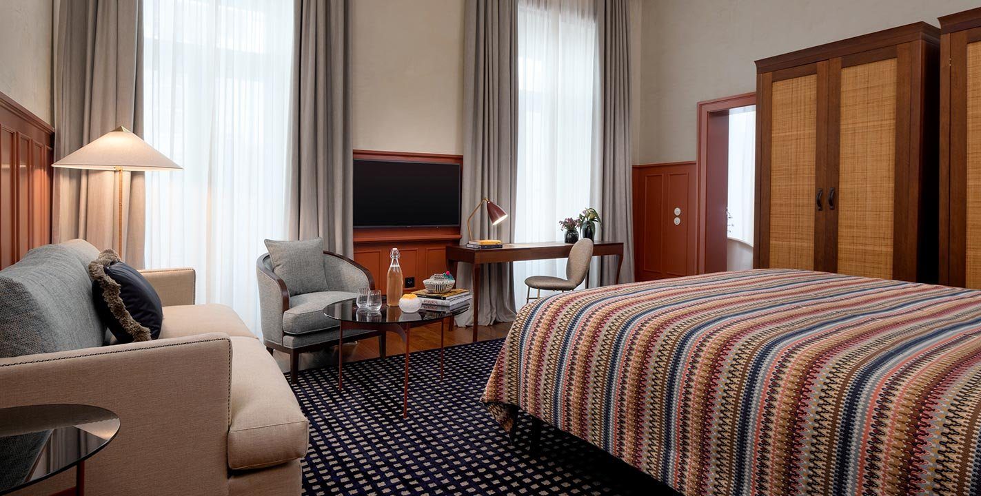 Patterned bedspread, seating area and tall windows in a Bairro Alto Hotel Prestige Chiado room.