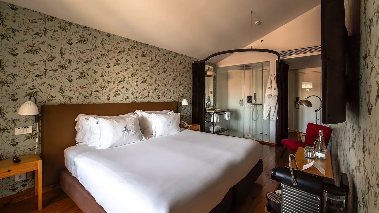 Lisboa Carmo Premium bedroom with botanical wallpaper, red chair and glazed shower enclosure.