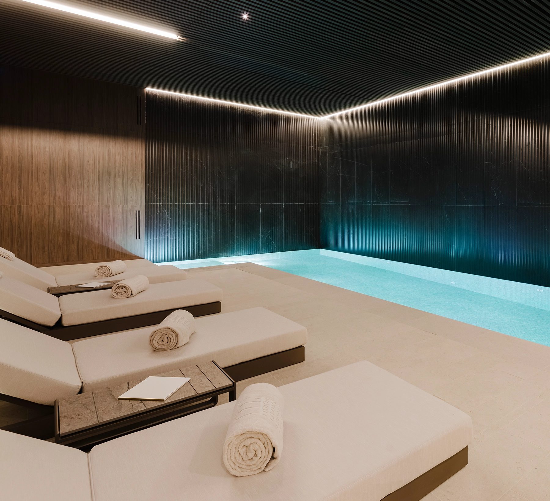 Lisbon Chiado Hotel & Spa’s indoor pool beside pale loungers and dark ribbed walls.