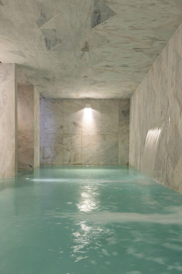 Empty marble-lined indoor relaxation pool at Lisboa Pessoa Hotel.