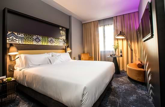 Down to Earth bedroom with patterned headboard and purple lighting at NYX Hotel Madrid.