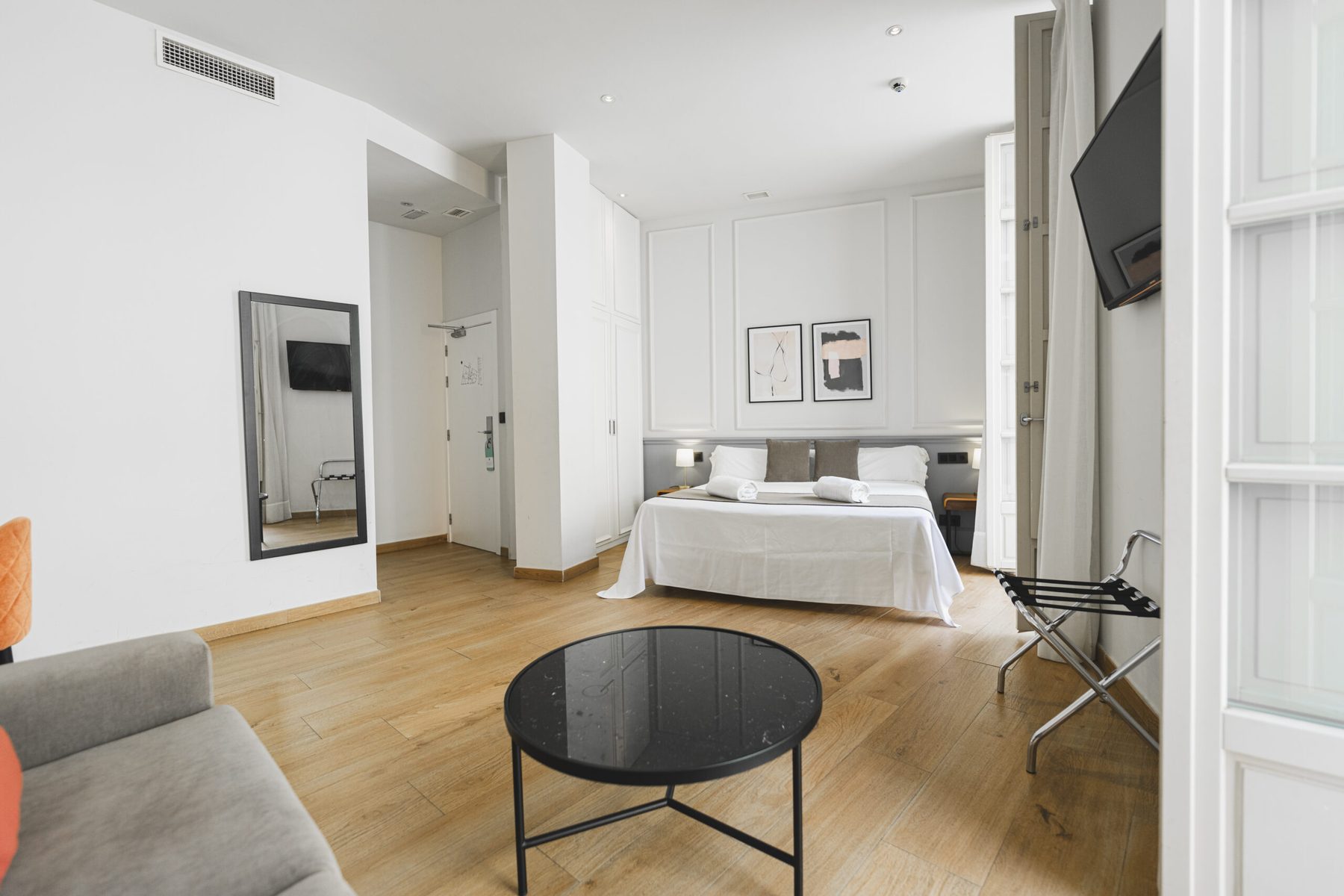 Double bed, wood floor, desk and sofa area in a bright hotel room.