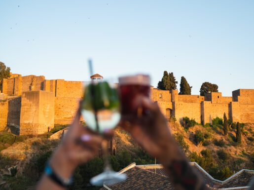 Two cocktail glasses held in front of the Alcazaba walls from the rooftop bar.