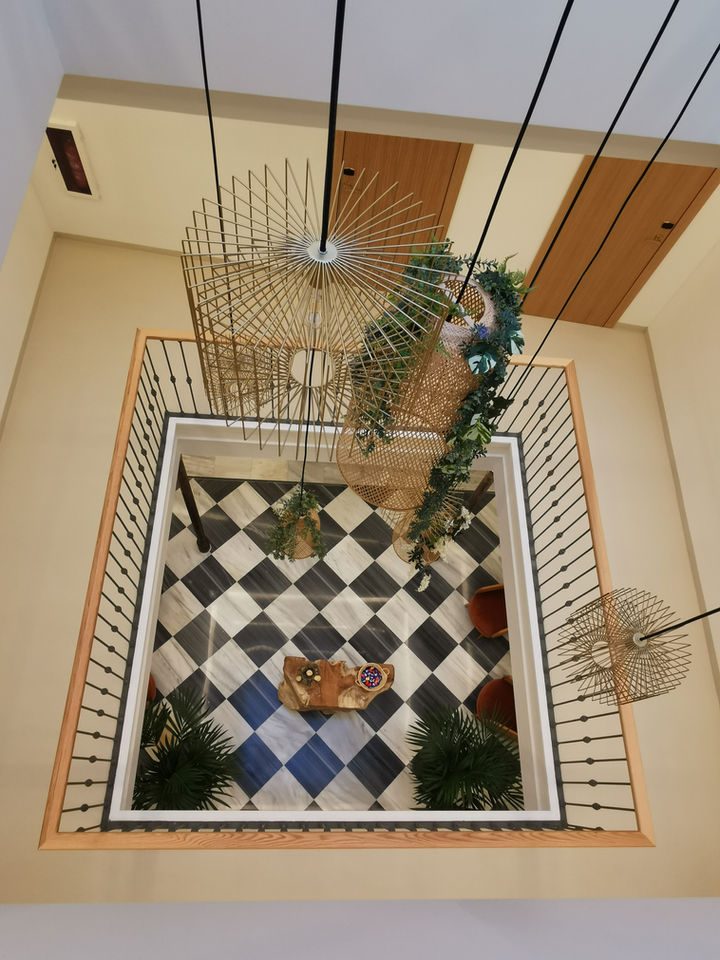 Hanging woven lamps and plants above a tiled atrium floor and stair rails.