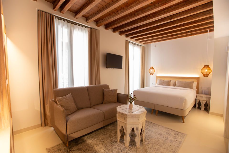 Double bed, sofa, wooden ceiling beams and a small carved table in a hotel bedroom.