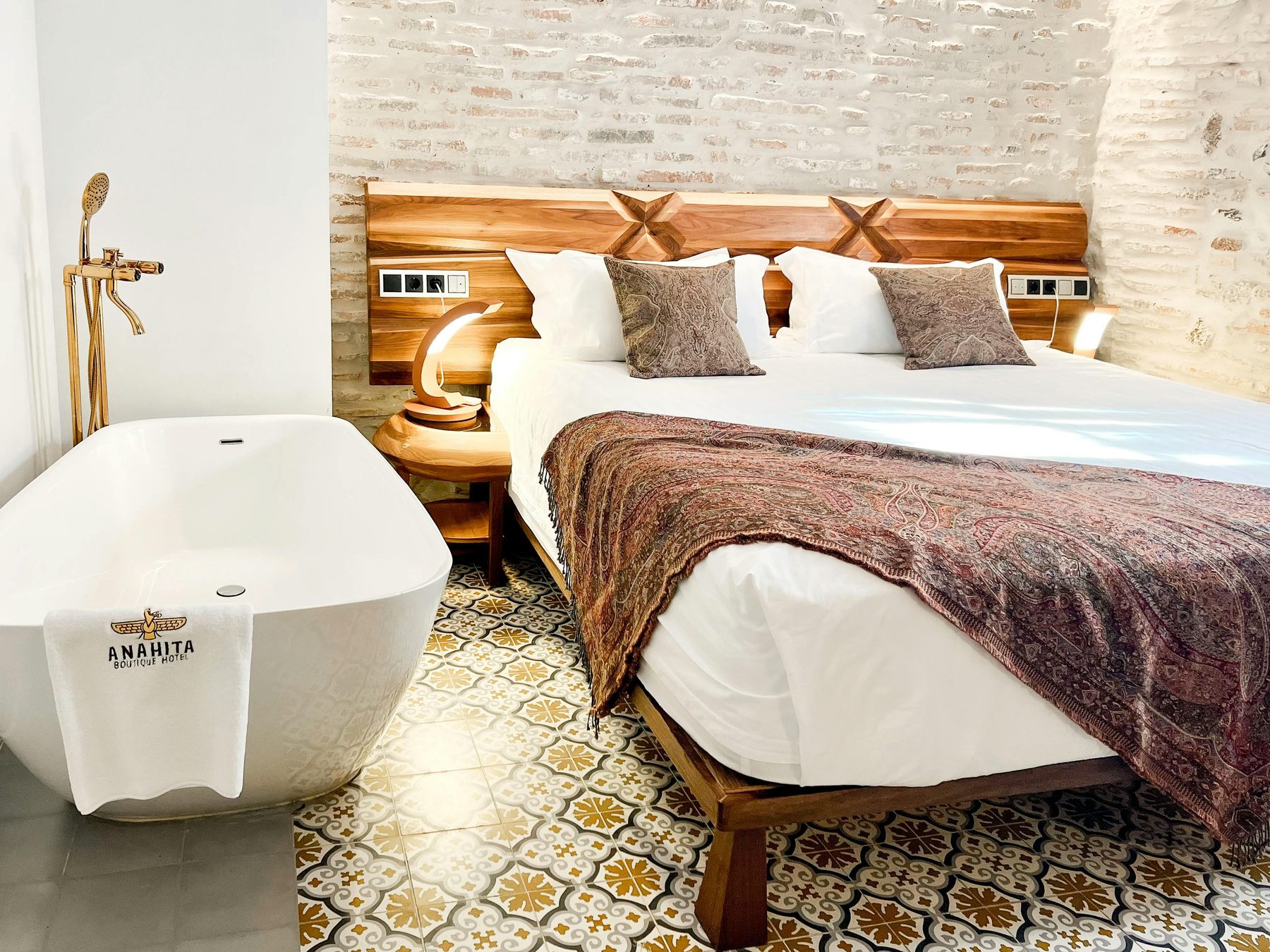 Double bed against exposed masonry with a freestanding white tub beside it.