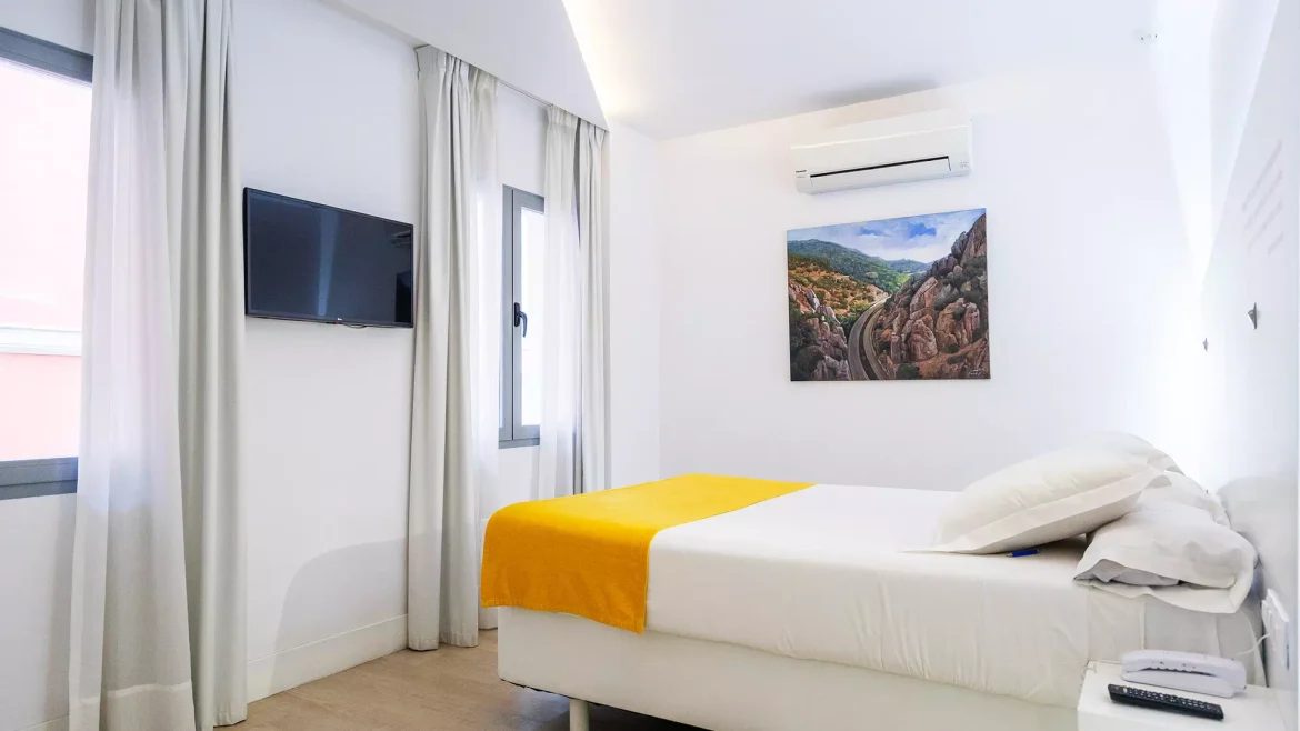 Light hotel bedroom with yellow bedding, a television and a curtained window.