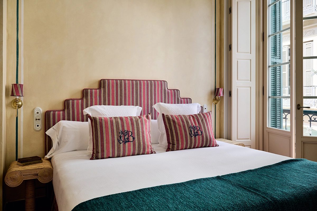 Striped upholstered headboard, double bed and tall shuttered doors in a Málaga Superior room.