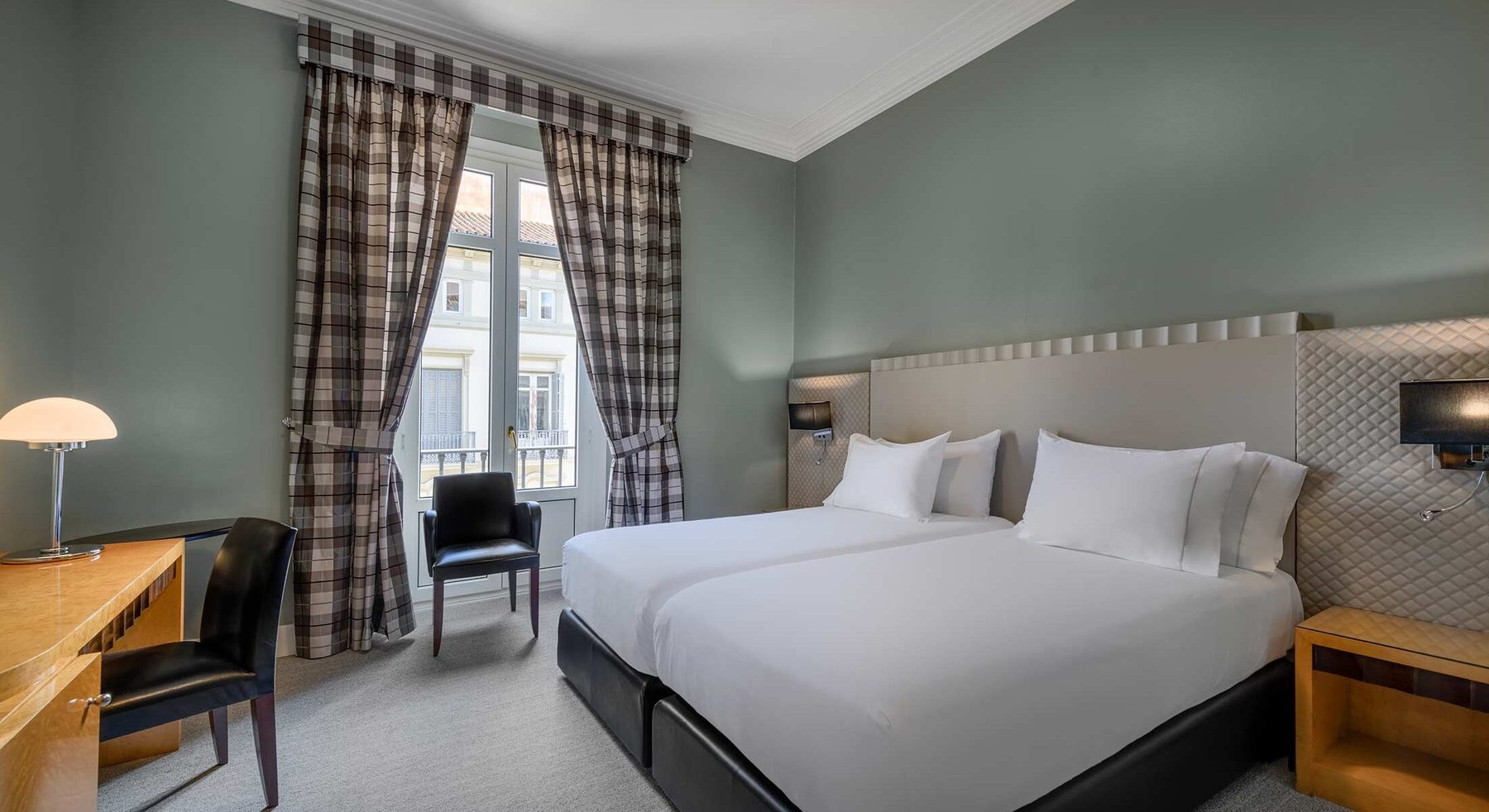 Twin beds, desk and a tall street-facing window in a Standard Double room.