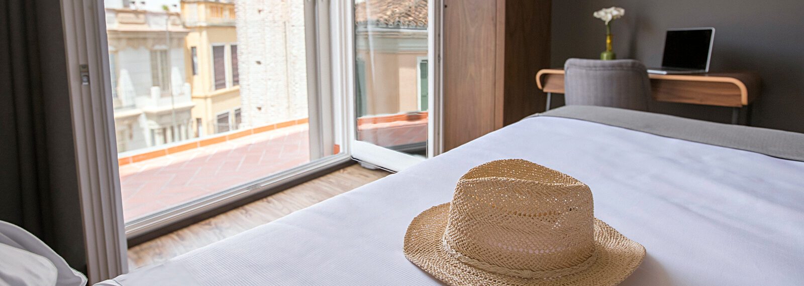 Hotel bed beside open balcony doors and historic street façades.