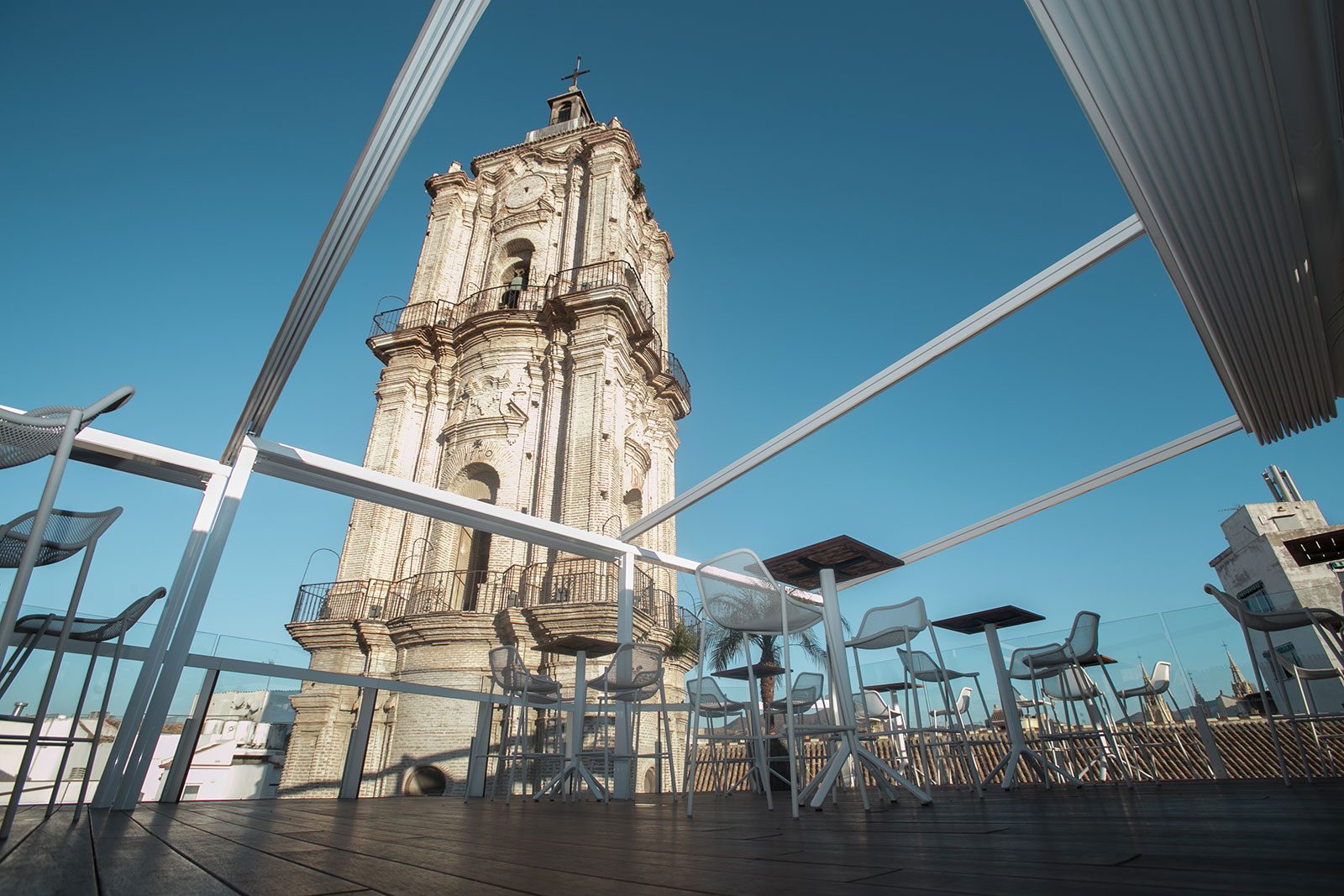 Rooftop terrace tables and stools beneath a canopy beside the San Juan church tower.