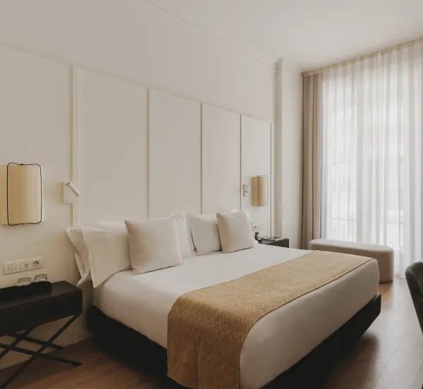 Cream-coloured double bed beside a tall curtained window in a Superior room.