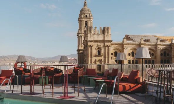 Pool water and metal pool ladder in front of red terrace seating and Málaga Cathedral.