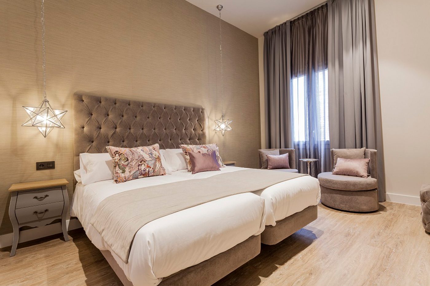 Tufted headboard, two adjoining mattresses, armchairs and tall curtains in a Superior room.