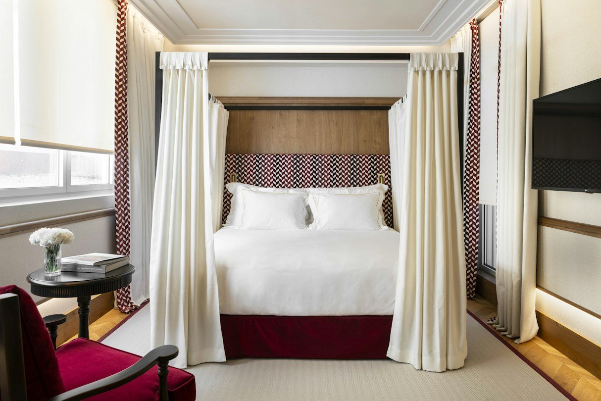 Canopy bed with red patterned textiles and a tall window in a Solecio Double.