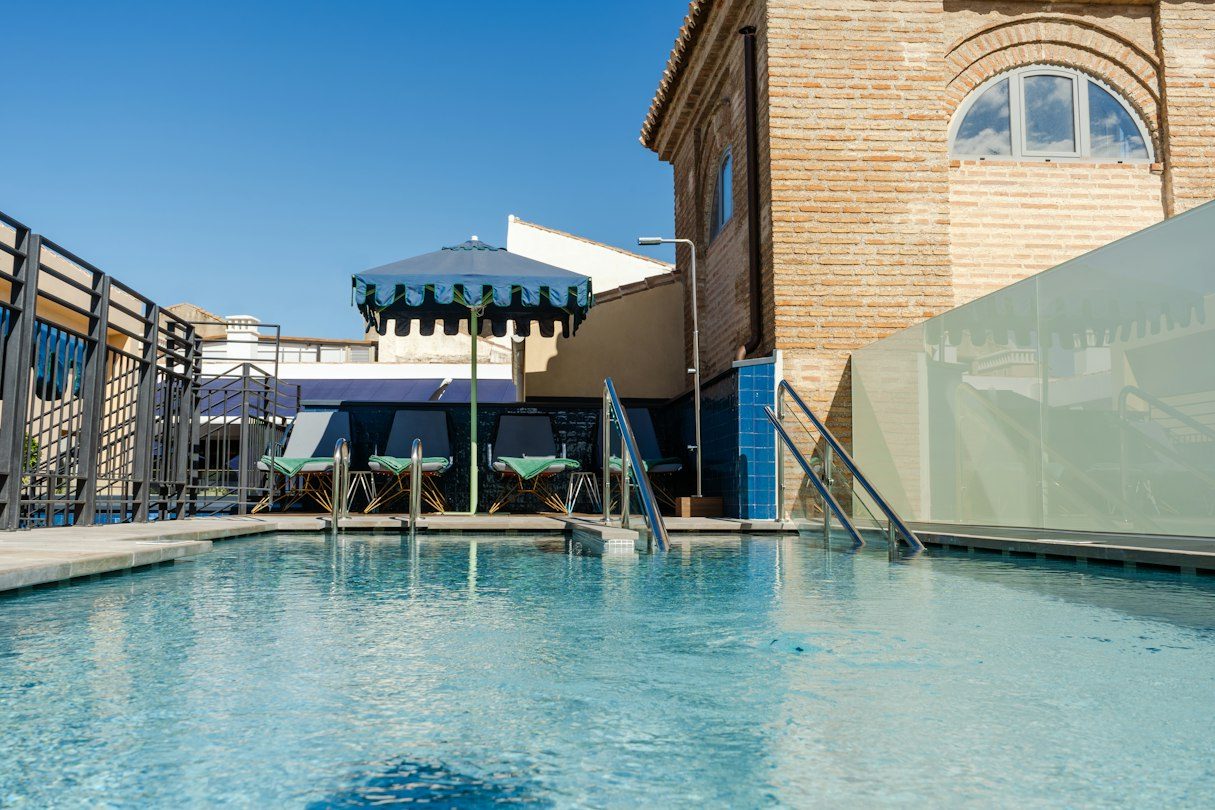 Rooftop swimming pool with a metal ladder, loungers and a brick rooftop structure.