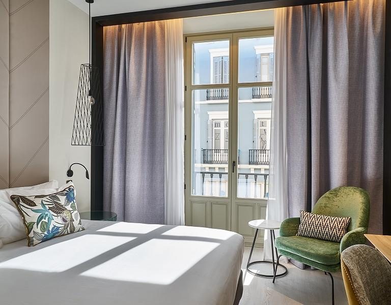 Bed, green armchair and tall glazed street-facing doors in a Vincci city-view room.