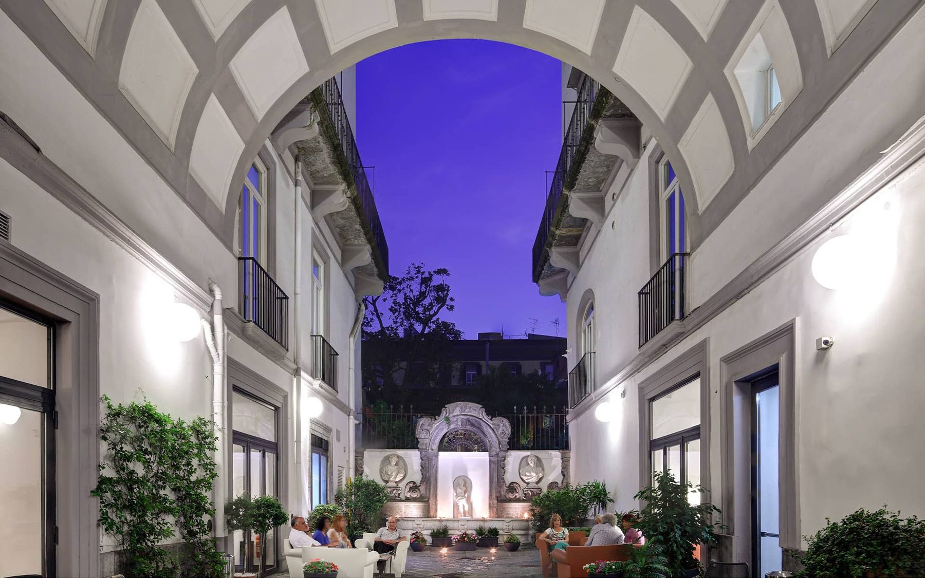 Illuminated courtyard with tables beneath a tall archway.