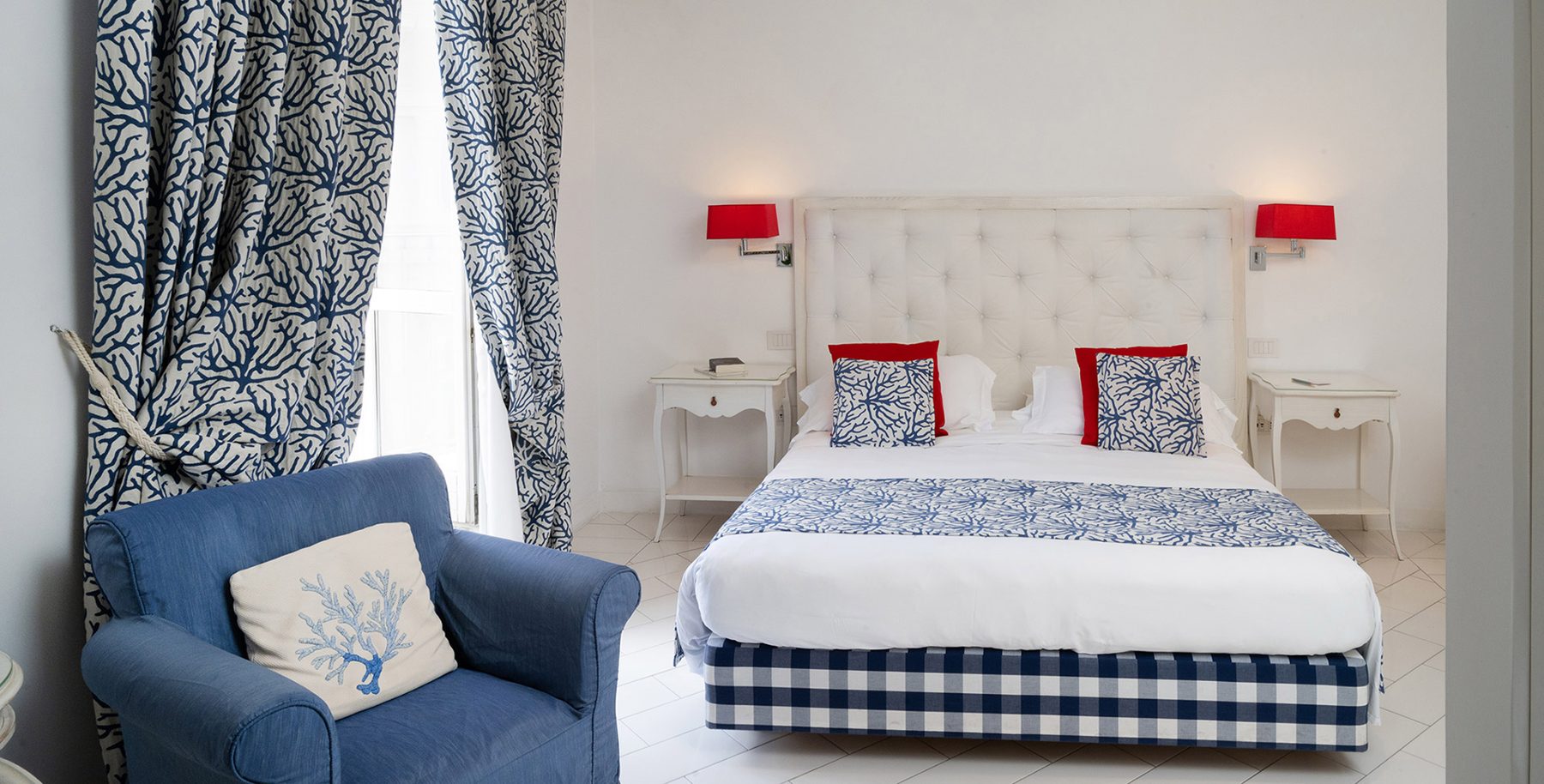 White bedroom with blue patterned fabrics and an armchair.